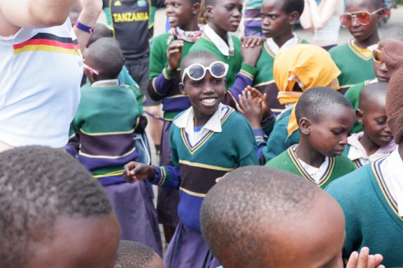3 Happy, so heißt auch das Mädchen Ein Mädchen steht glücklich in der Mitte, um sie herum viele Kinder. Sie trägt eine Sonnenbrille auf dem Kopf.