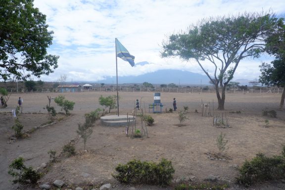 7 eingezäuntes Schulgelände Ein Schulgelände mit einem Zaun geschützt. Eine Tansania-Flagge weht in der Mitte. Kinder spielen im Freien