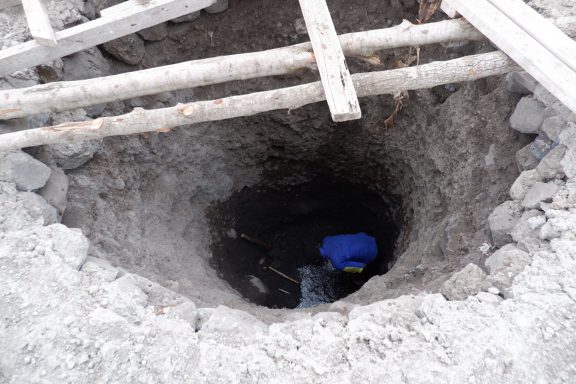 4 erstes Wasser in acht Meter Tiefe EIn tiefes Loch in dem ein Mann steht, man sieht Wasser am Grund.