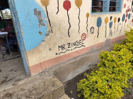 1 Außerhalb eines Klassenraums der Lekrimuni Primary School Man sieht Malereien an einer Hauswand. Luftballons und den Namen Mr. Zingel