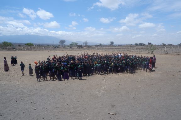 8 Versammlung von Schülern und Schülerinnen der Primary School Eine Gruppe von ca. 300 Kindern jubeln auf einem eingezäunten Gelände
