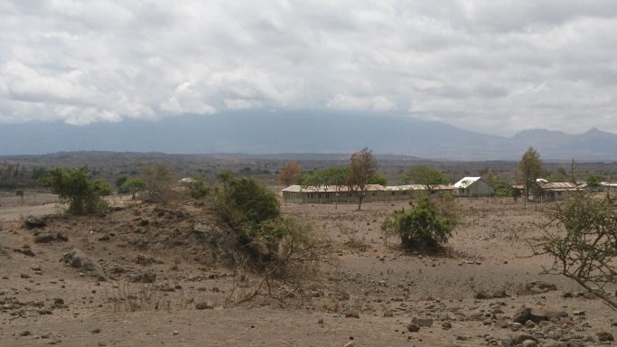 1 Lekrimuni vor dem Mt. Meru in der Trockenzeit Eine große freie Fläche mit einem Berg im Hintergrund. Sehr trockener Boden